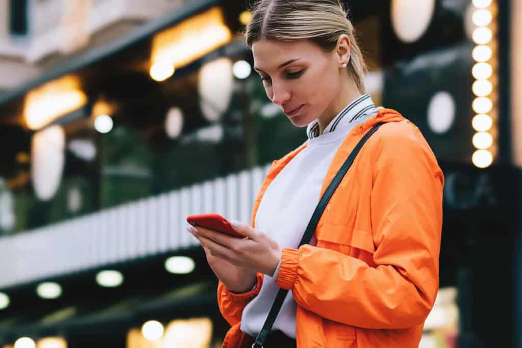 Woman using smartphone for social media management in urban setting.